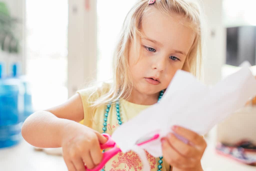 little girl cutting paper with pink scissors